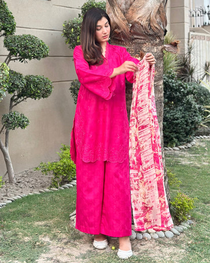 Woman in a pink traditional outfit holding a patterned scarf outdoors.